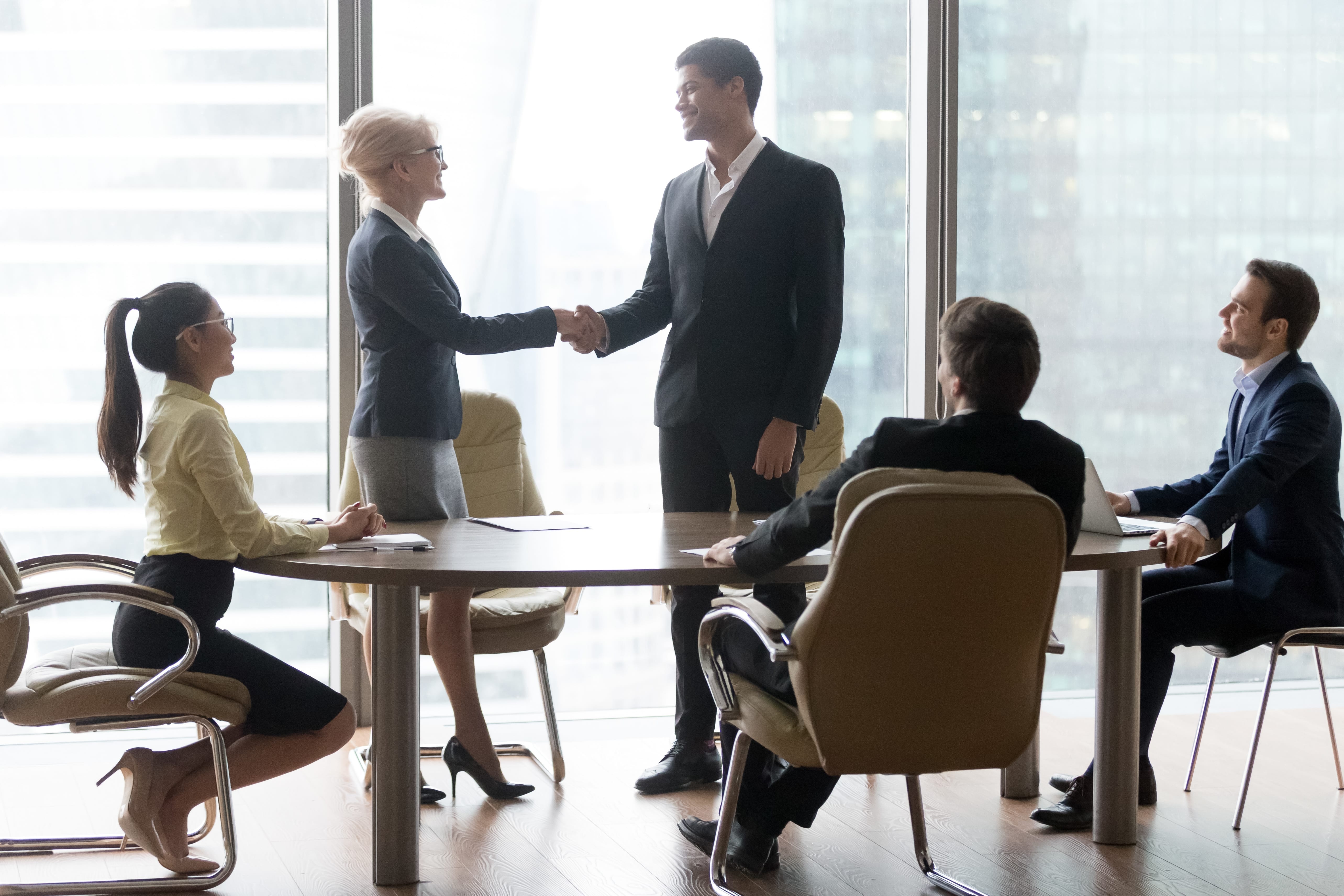 Happy middle aged boss leader handshaking african businessman welcoming greeting new partner at team meeting in boardroom, diverse executives shake hand as promotion respect and rewarding concept